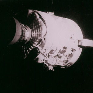 The Apollo 13 service module in black and white. The top half is smooth and covered, but the bottom half has exposed interior.