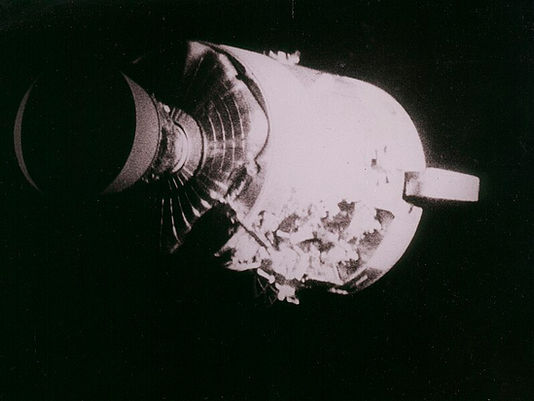 The Apollo 13 service module in black and white. The top half is smooth and covered, but the bottom half has exposed interior.
