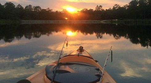 Orange kayak with two fishing poles floating in still water along the coast of Isle Madame as the sun sets