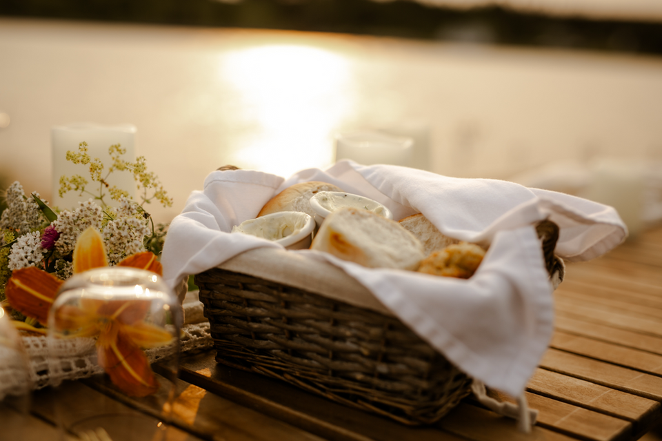 a basket of food on an outdoor dining table overlooking the ocean at sunset