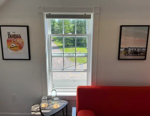 The Beatles art on the walls of a room with a window and red couch overlooking trees, grass and a gravel drive 