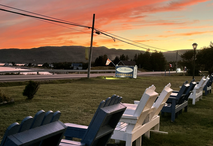lawn chairs lined up on the front lawn of sea breeze cottages next to the ocean as the sun sets