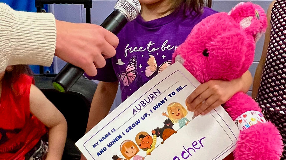 Two children with purple sunglasses pose in a classroom. One holds a pink stuffed toy and sign reading "a teacher." Background has colorful decor.