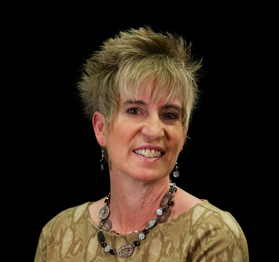 Smiling woman with short hair in a patterned beige top, wearing a necklace. Black background.