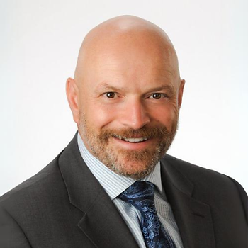 Man with beard, dressed in a tie and suit, smiles.
