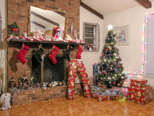 fireplace decorated with stockings , surrounded by Christmas tree and wrapped presents