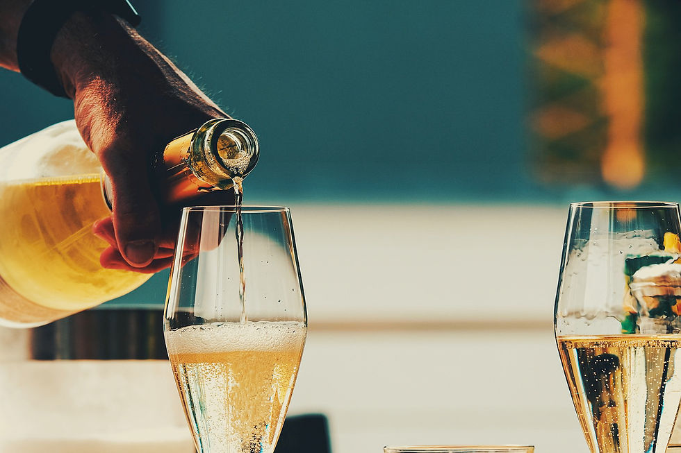 Hand pours sparkling wine into a glass, with another filled glass nearby. Warm light, bubbly texture, and a blurred, colorful background.
