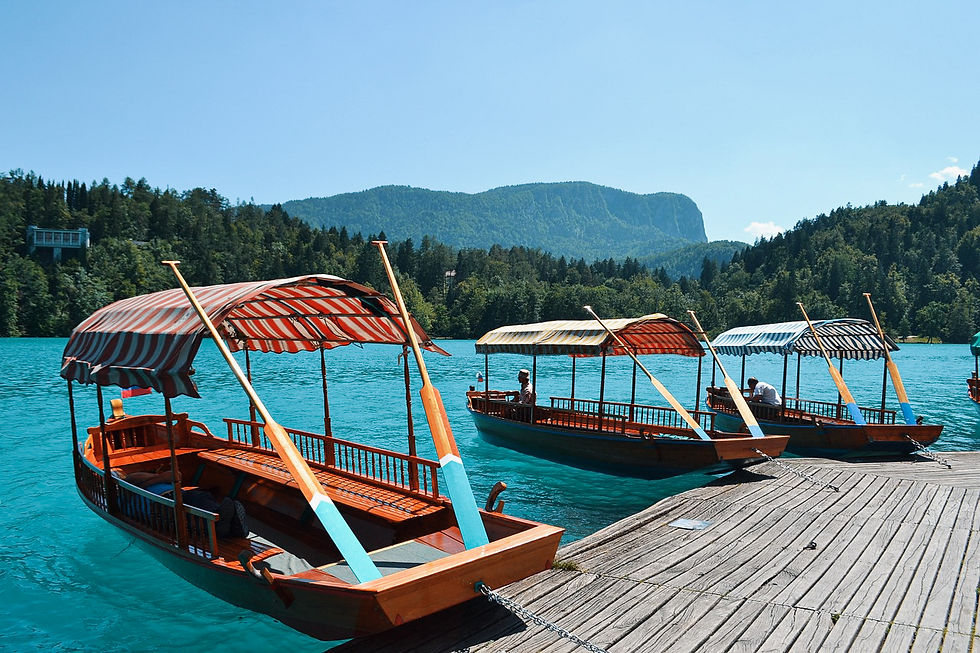 Three wooden boats with striped canopies are docked on a serene turquoise lake, surrounded by forested mountains under a clear blue sky.