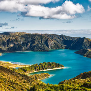 Lush green mountains surround a vibrant blue lake under a partly cloudy sky at Sete Cidades in São Miguel on the Azores. The serene landscape exudes tranquility and natural beauty.