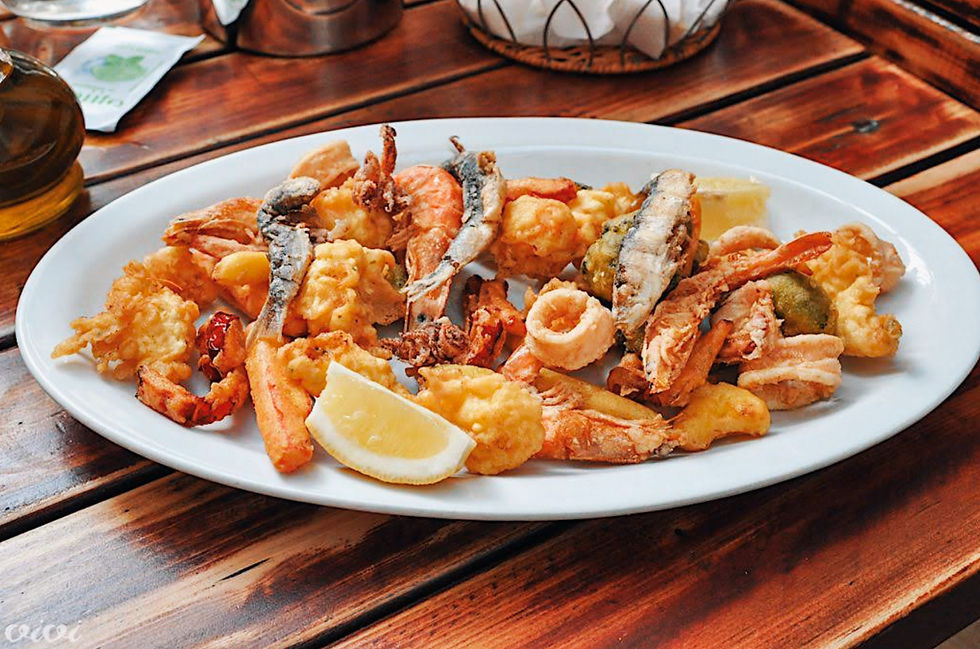 A white plate with fried seafood, lemon slices on a wooden table. Background has a metal basket and glass bottle. Warm, rustic setting.