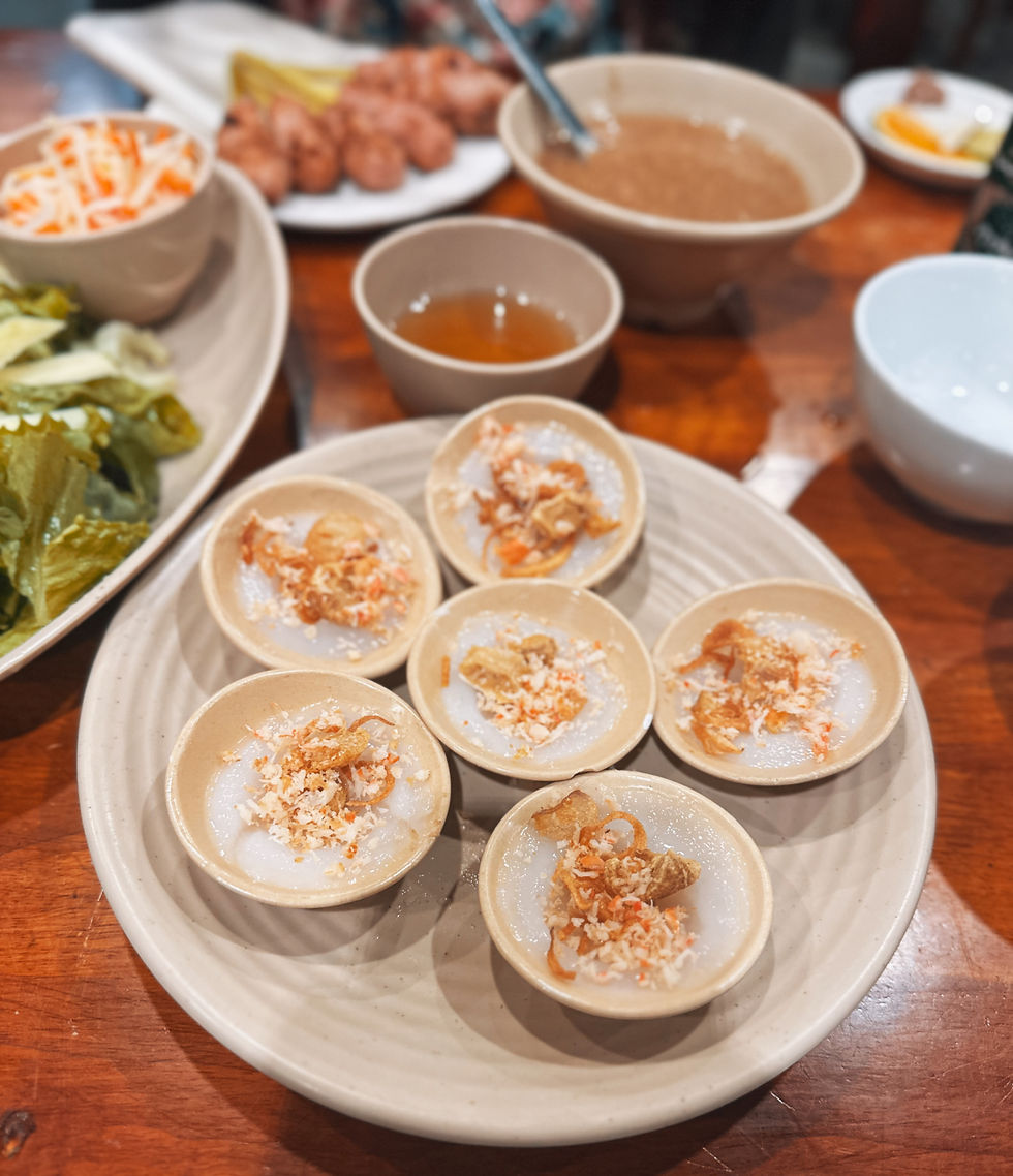 Small ceramic bowls of savory Vietnamese rice cakes on a wooden table, garnished with crispy onions and served with herbs and sauce.