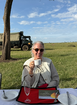 Laurel Louderback sitting at a table outside drinking coffee on safari in Africa