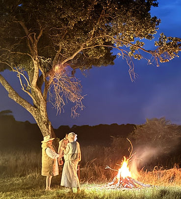 Laurel Louderback standing with two other people talking in front of a campfire at night in Africa