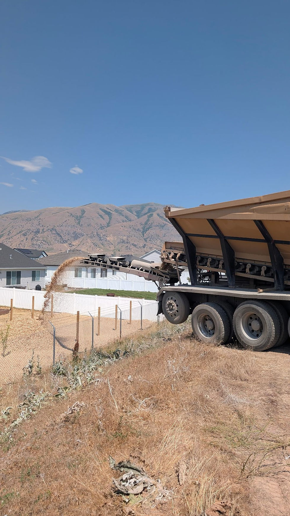 Conveyor truck shooting bark and wood chips over a fence into a backyard in Hyrum, Utah