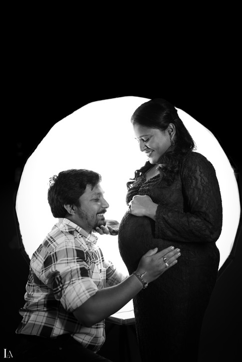 Black and white artistic portrait of a husband admiring his pregnant wife's baby bump during a studio maternity session in Vizag.