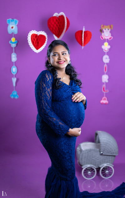 Pregnant woman smiling in a blue lace gown during an indoor studio maternity photoshoot at LensAction Photography in Visakhapatnam.