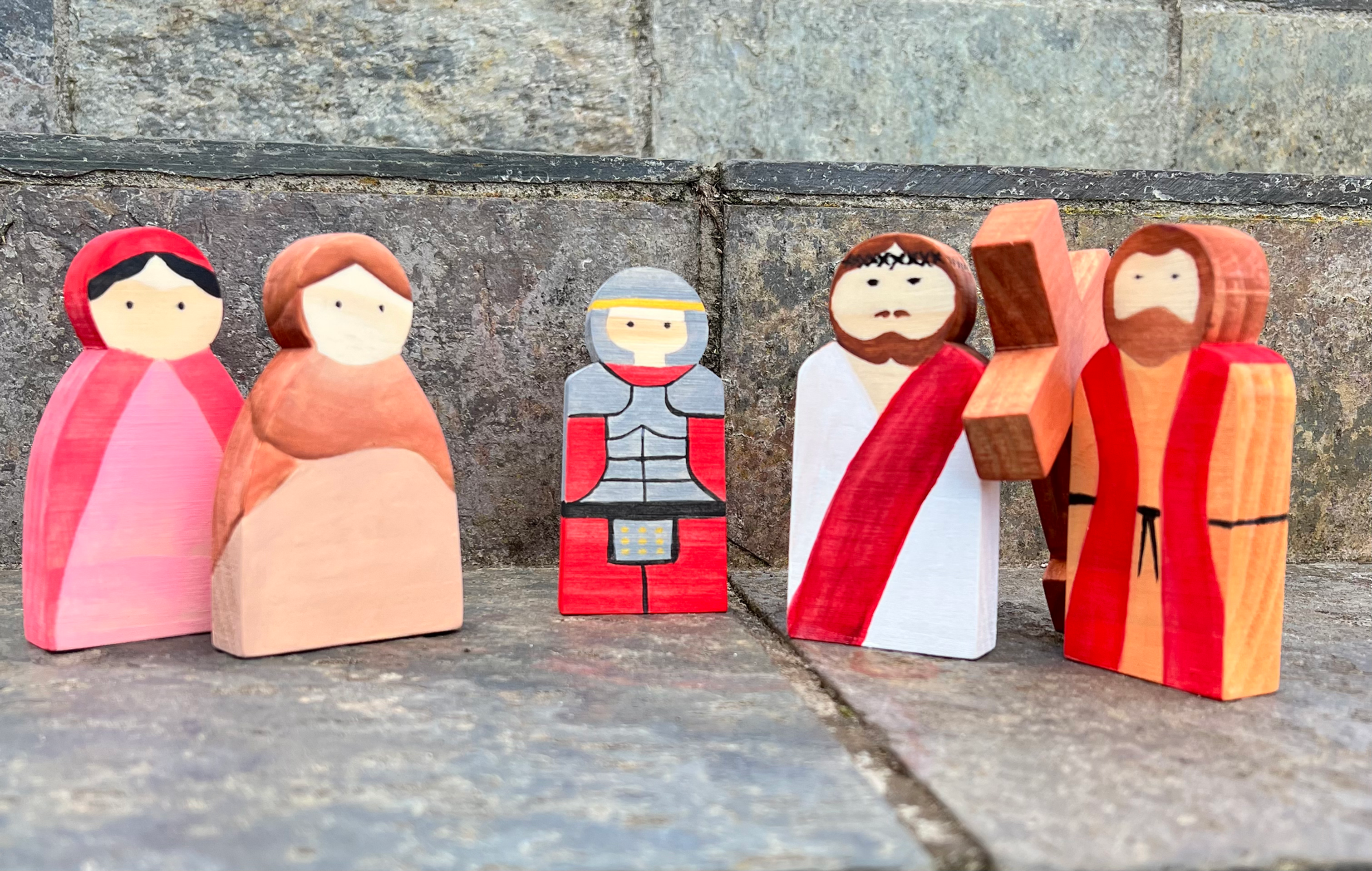 Wooden figures of people standing with a cross on a stone background.