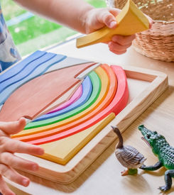 Child playing with wooden rainbow toy and animal figures on table.