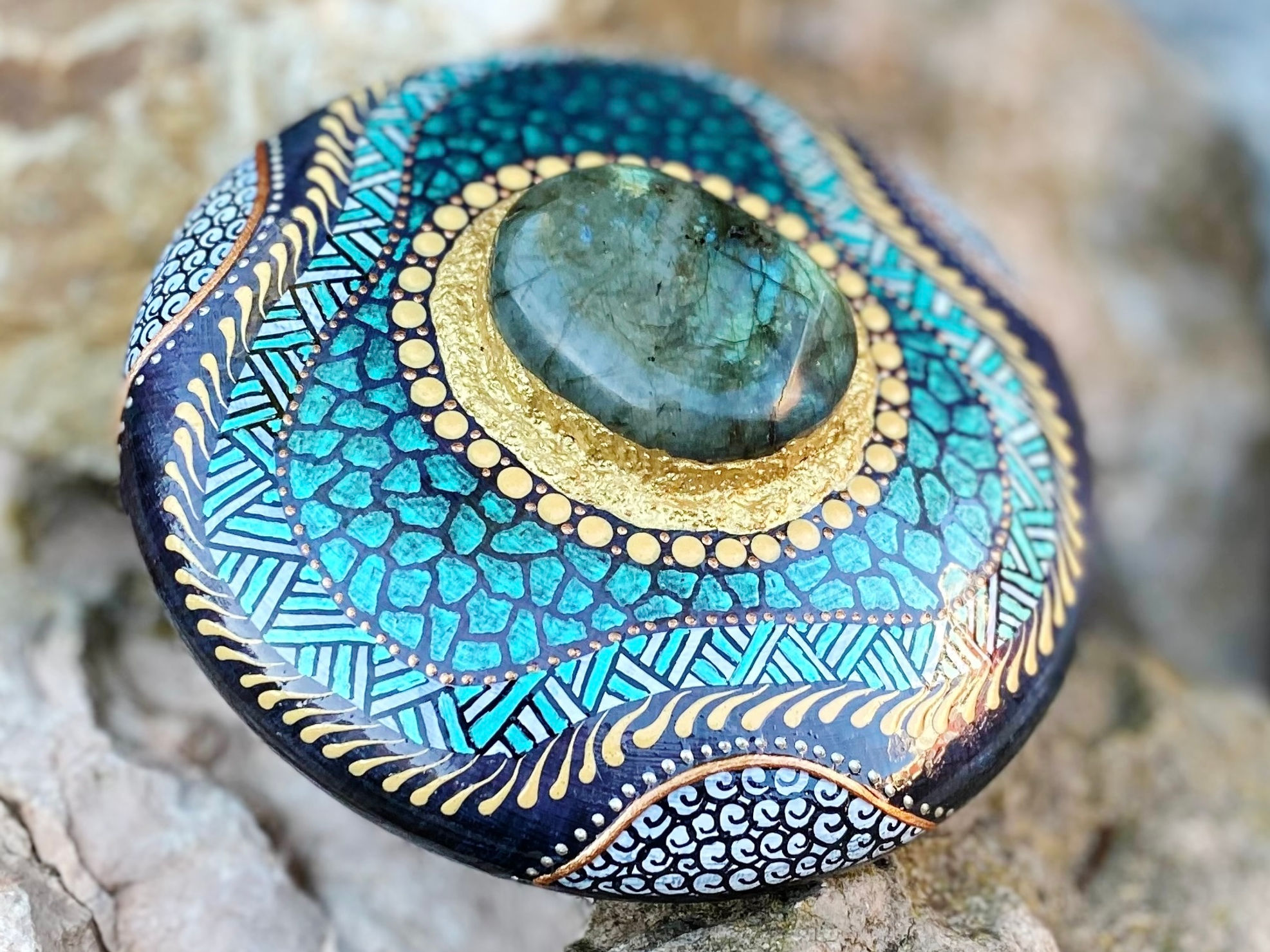 Handbeschilderde spirituele mandala-steen met labradoriet in het midden, versiert met groene en goudkleurige patronen.