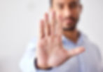 A person extends an open hand toward the camera, suggesting a stop gesture. The background is blurred, and they wear a light blue shirt.