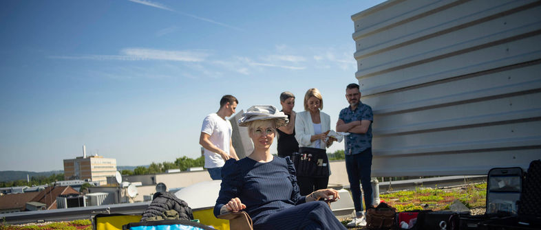 Frau sitzt auf Dachterrasse mit Team im Hintergrund