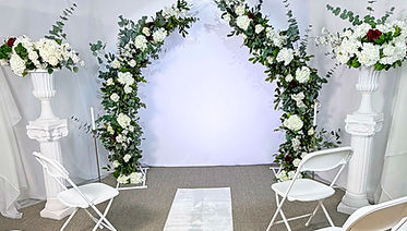 Indoor wedding setup for elopement with floral arch, draped backdrop, candles, and seating