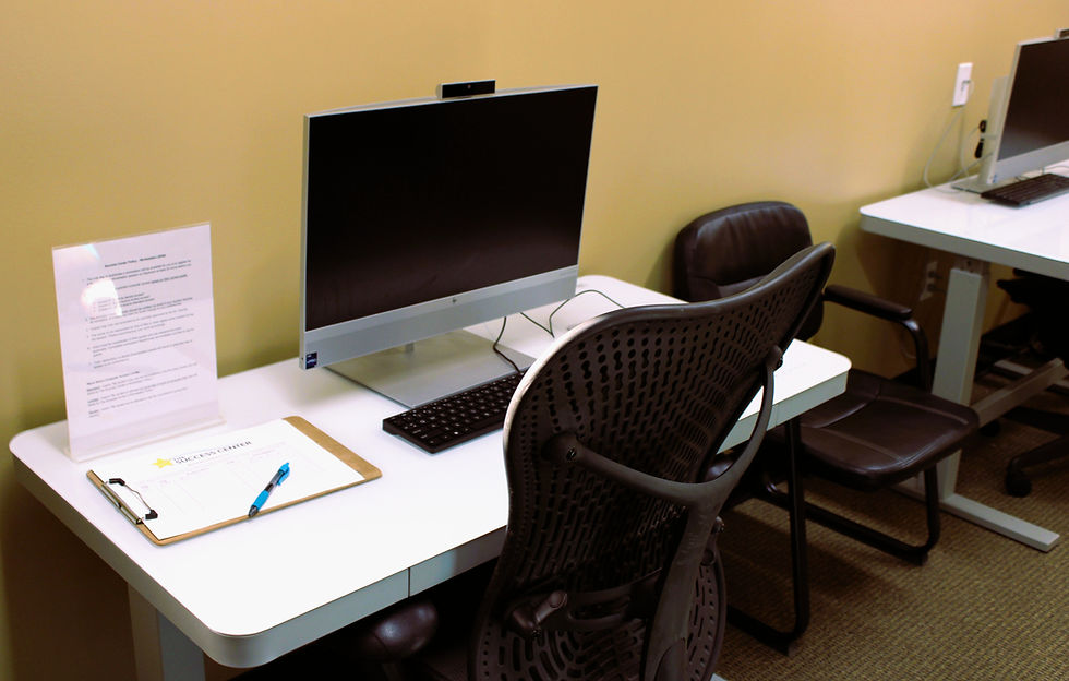 A workstation with an adjustable height desk, computer, keyboard, chair, pen, paper, and sign-in sheet is ready to be used at the Success Center at Ice in Paradise