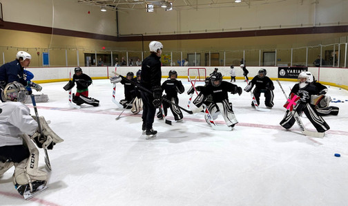 A group of young goalies practice transitioning from standing to butterfly pose while coaches give pointers.