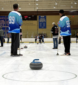 Participants look on as a stone is thrown down the ice.
