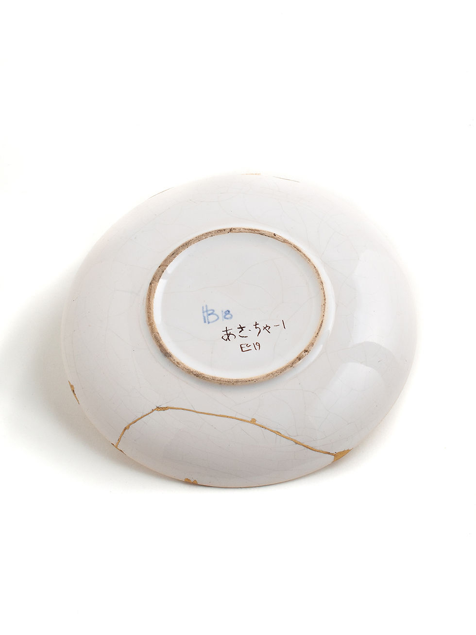 Miniaturbild: Keramik-Untertasse mit Kintsugi repariert. unterseite. Cremeweiß mit hellblauem Design. Brüche mit echtem Gold veredelt.