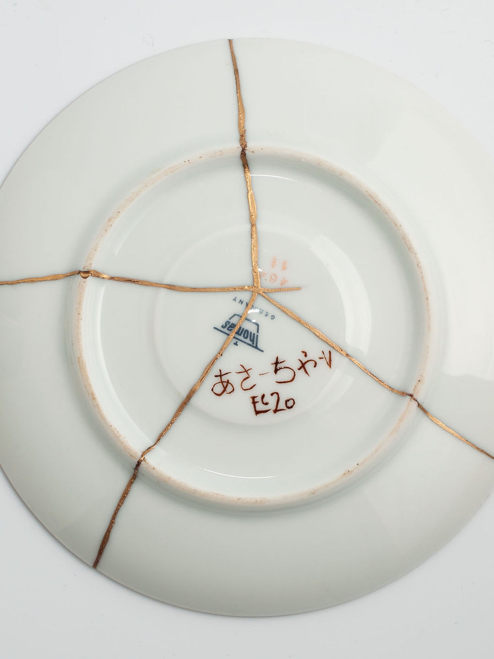 Thumbnail: zweiteiliges Porzellan-Teeservice mit Kintsugi repariert. Unterseite der Untertasse. Brüche mit echtem Gold veredelt.