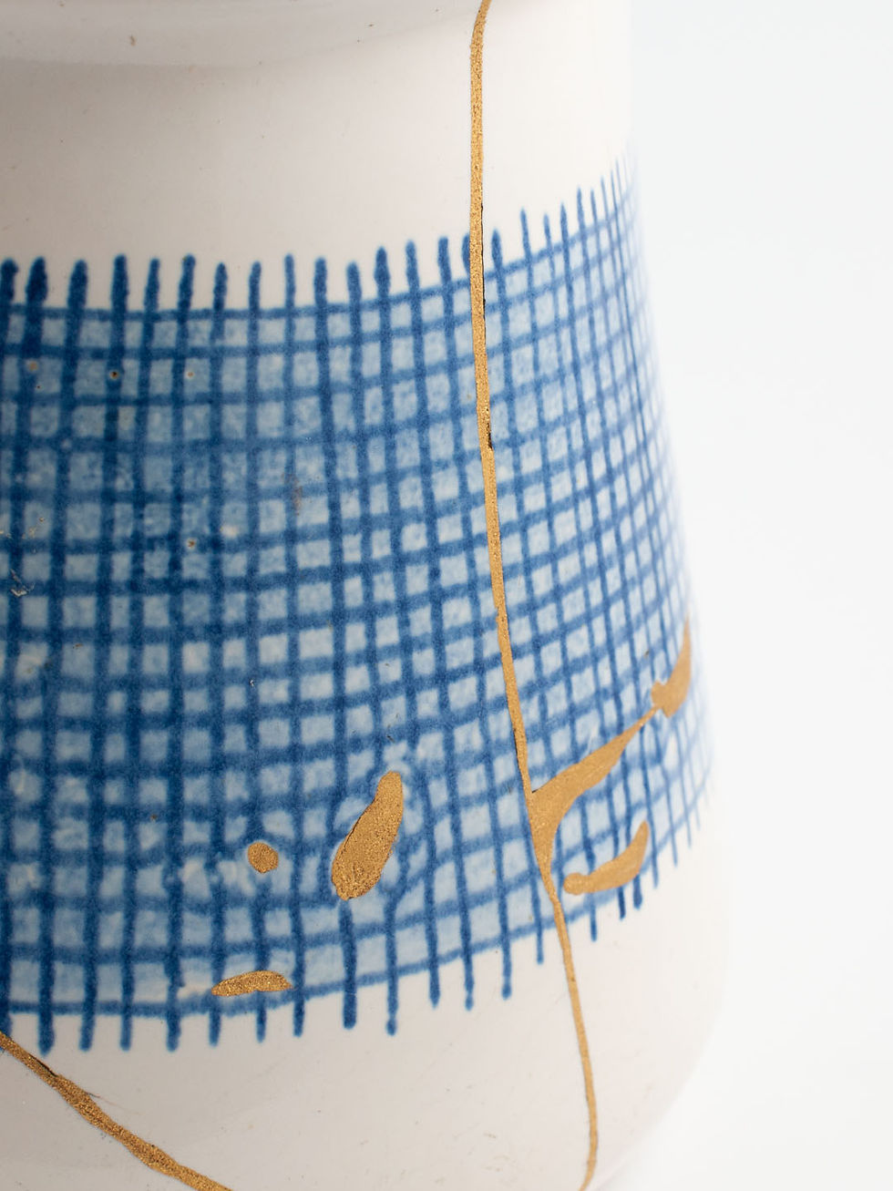 Thumbnail: Detail von Keramikkrug in Cremeweiß mit blauem Schraffurmuster, repariert mit Kintsugi. Brüche mit echtem Gold veredelt.