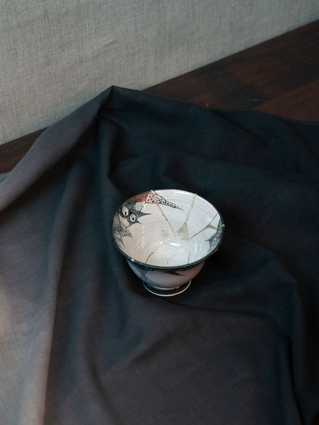 Eine Kintsugi-Keramikschale mit einem Furoshiki-Tuch in einem Farbverlauf von Dunkelblau zu Grau.