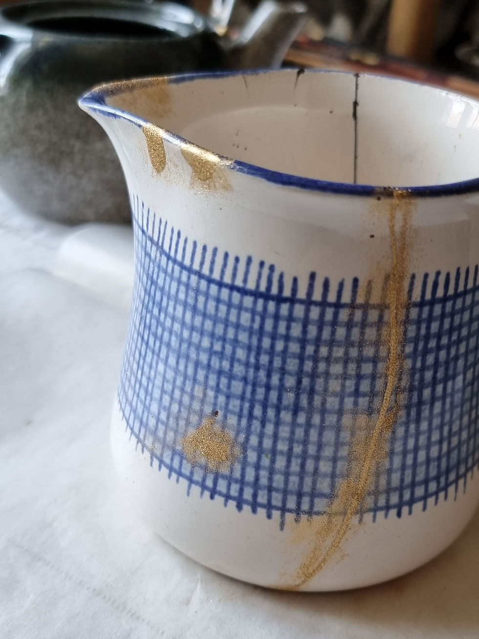 Miniaturbild: Keramikkrug in Cremeweiß mit blauem Schraffurmuster, Verfahren zum Auftragen der Goldveredelung.