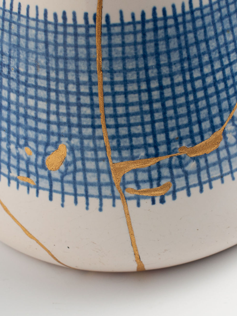 Thumbnail: Detail von Keramikkrug in Cremeweiß mit blauem Schraffurmuster, repariert mit Kintsugi. Brüche mit echtem Gold veredelt.