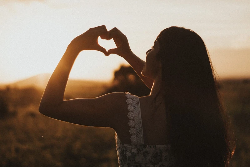 LADY MAKING HAND SHAPE HEART WITH HER HANDS INTO THE SUNSET