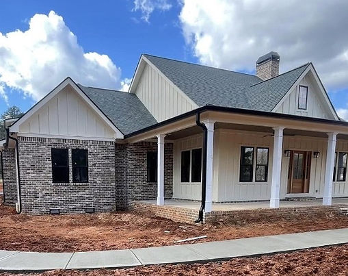 Residential concrete driveway and front sidewalk installation at a newly constructed home with a covered porch and brick exterior.