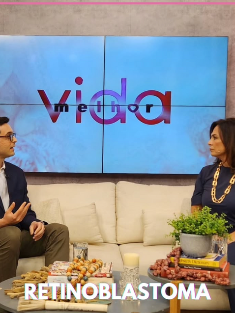 Dr. Felipe Baccega, oftalmologista, em entrevista no programa Vida Melhor, falando sobre saúde ocular, sentado em um sofá ao lado da apresentadora, com a logo do programa exibida ao fundo.