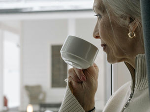 Mulher idosa tomando café enquanto observa a paisagem, simbolizando os desafios da visão central comprometida pela degeneração macular relacionada à idade (DMRI).