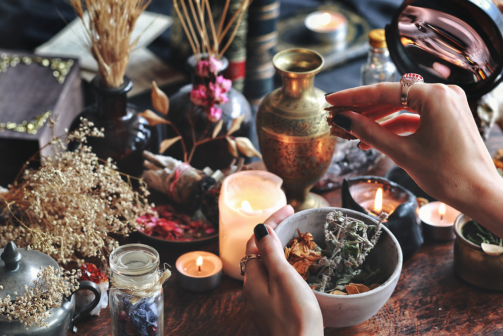 woman's hands holding a bowl of herbs, candles and brass ornaments