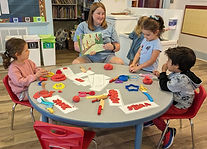 Children gathered around the play-dough table with Teacher Michele