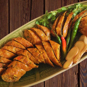 Geschnittene Chiang Mai-Wurst, serviert mit Chilis, Ingwer und Koriander auf einer traditionellen Keramikplatte.