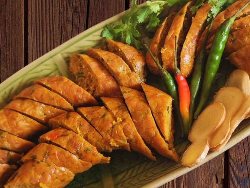 Geschnittene Chiang Mai-Wurst, serviert mit Chilis, Ingwer und Koriander auf einer traditionellen Keramikplatte.