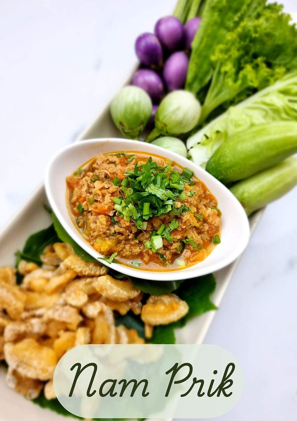 Bol de nam prik ong entouré de légumes crus, légumes cuits et couenne de porc frite, présenté comme un plateau traditionnel du Nord de la Thaïlande.