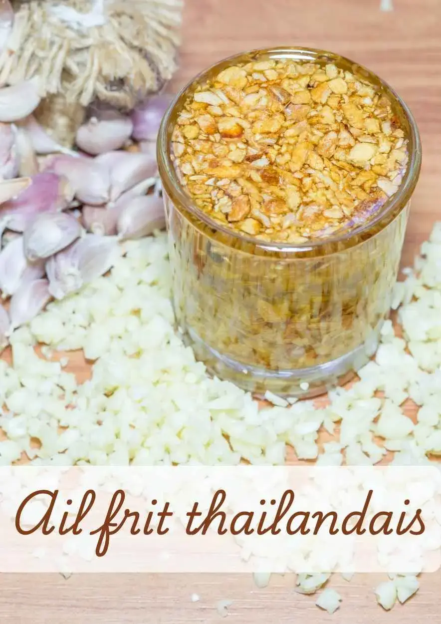 Thai fried garlic and garlic oil in a glass, surrounded by fresh garlic cloves and chopped raw garlic on a wooden board.