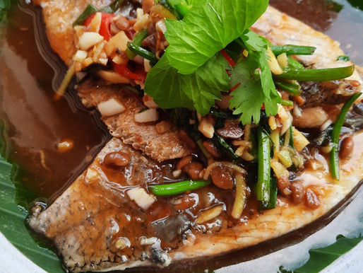 Assiette de poisson frit nappé d'une sauce tamarin et gingembre, garnie d'herbes fraîches, de piments rouges et d'aromates thaïlandais, servie sur une feuille de bananier