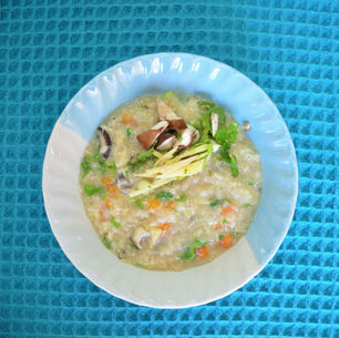 Bol de congee thaïlandais végétarien aux œufs, garni de champignons shiitake, de gingembre en julienne, de coriandre et de ciboule, servi dans un bol en céramique sur un tissu bleu.