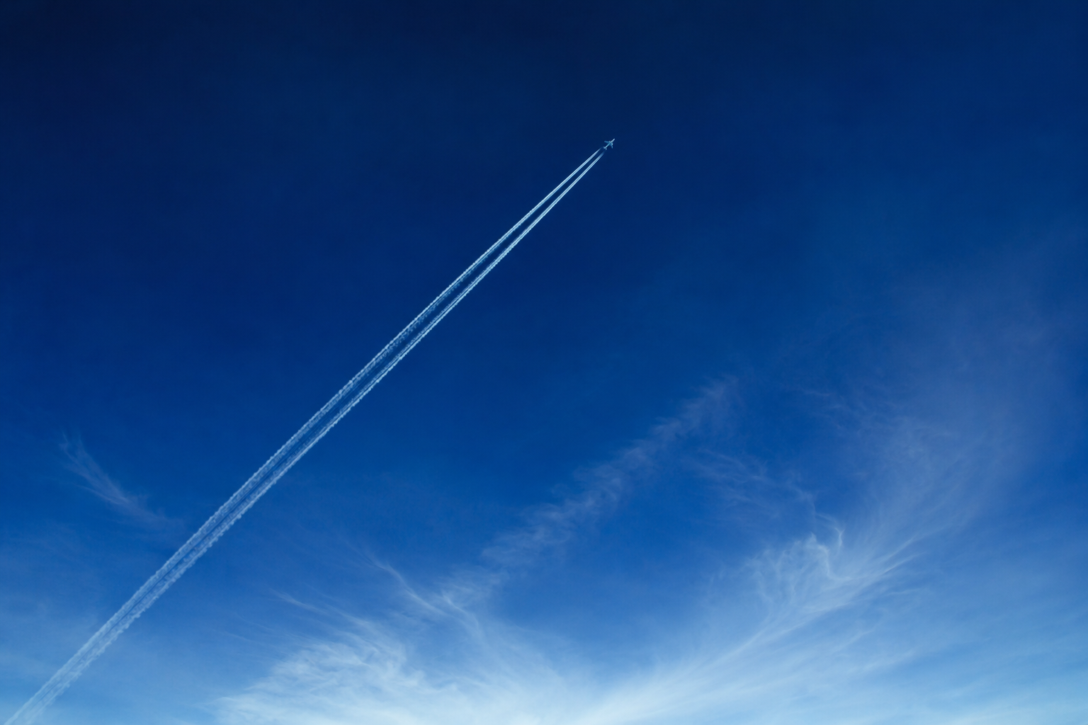 An anonymous aircraft at high altitude crossing a clear blue sky with contrails