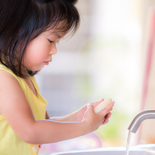 A young child is washing her hands at a sink, holding a bar of soap and focusing carefully on cleaning.