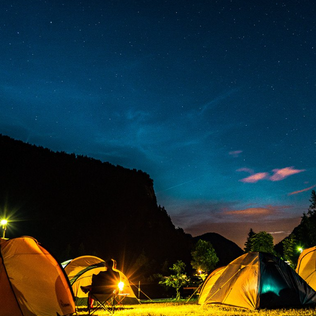 Tents glow under a clear night sky beside dark mountain silhouettes.